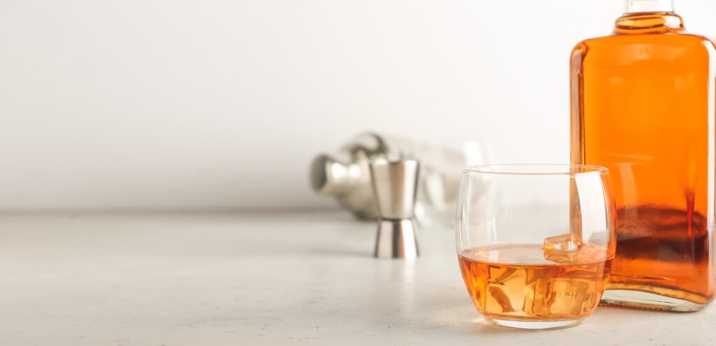 filled glass whiskey bottle and whiskey glass on a light background